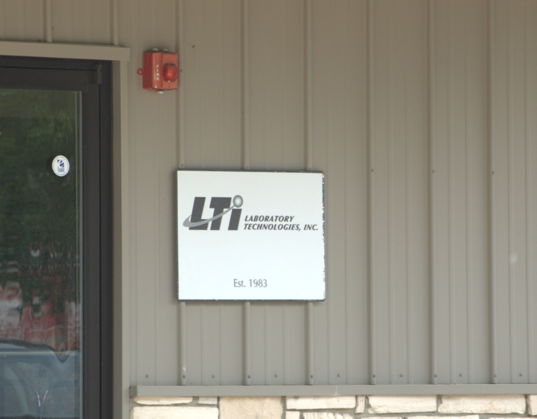 The LTI Laboratory Technologies, Inc. sign at 747 Herra Street, Elburn, IL — Est. 1983, weathered and scuffed from four decades on the wall