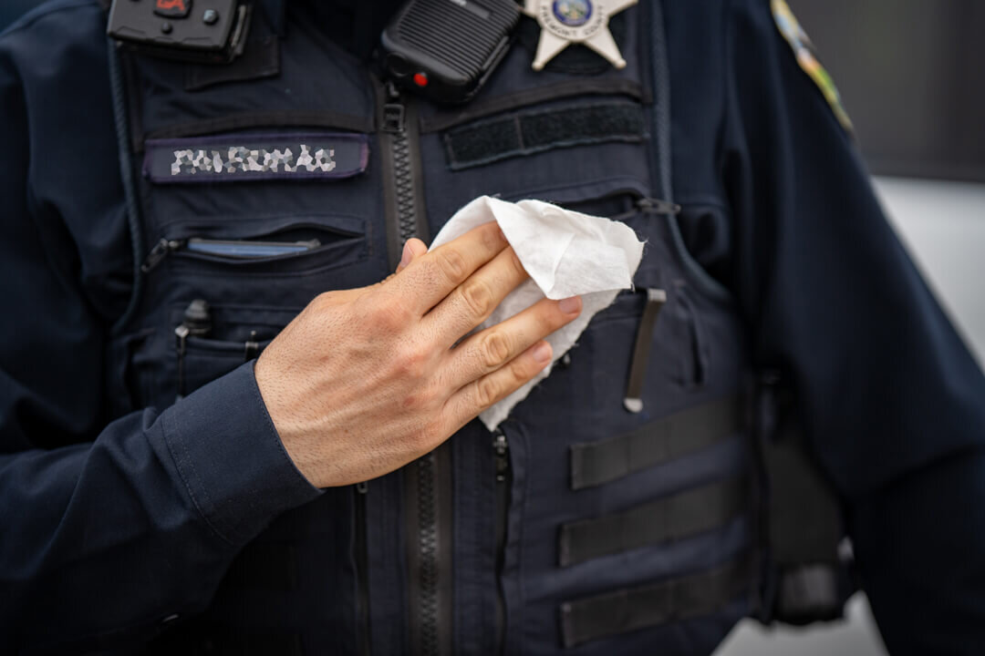Patrol officer with body camera and county sheriff badge wiping down the front of his duty vest with an S4FE-D® D.I.R.T. wipe after an exposure incident in the field.