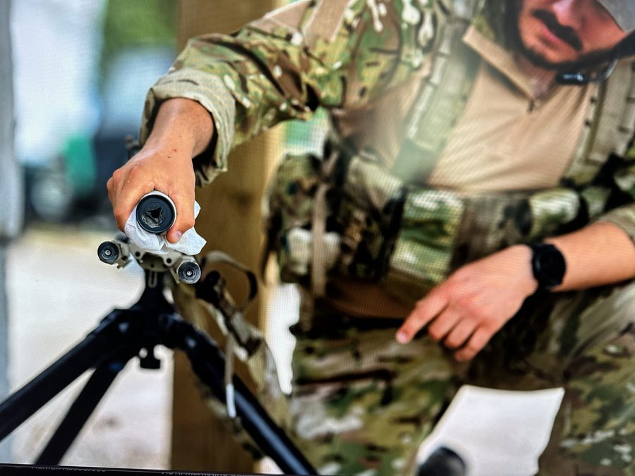 Operator using an S4FE-D® D.I.R.T. wipe on a precision rifle suppressor — surfactant chemistry lifts carbon, primer residue, and lubricant without harming the finish.