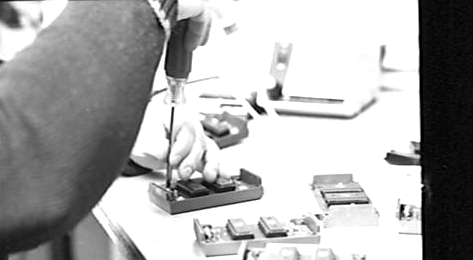 Close-up of hands assembling small electronic application modules at an LTI workbench, c. 1986
