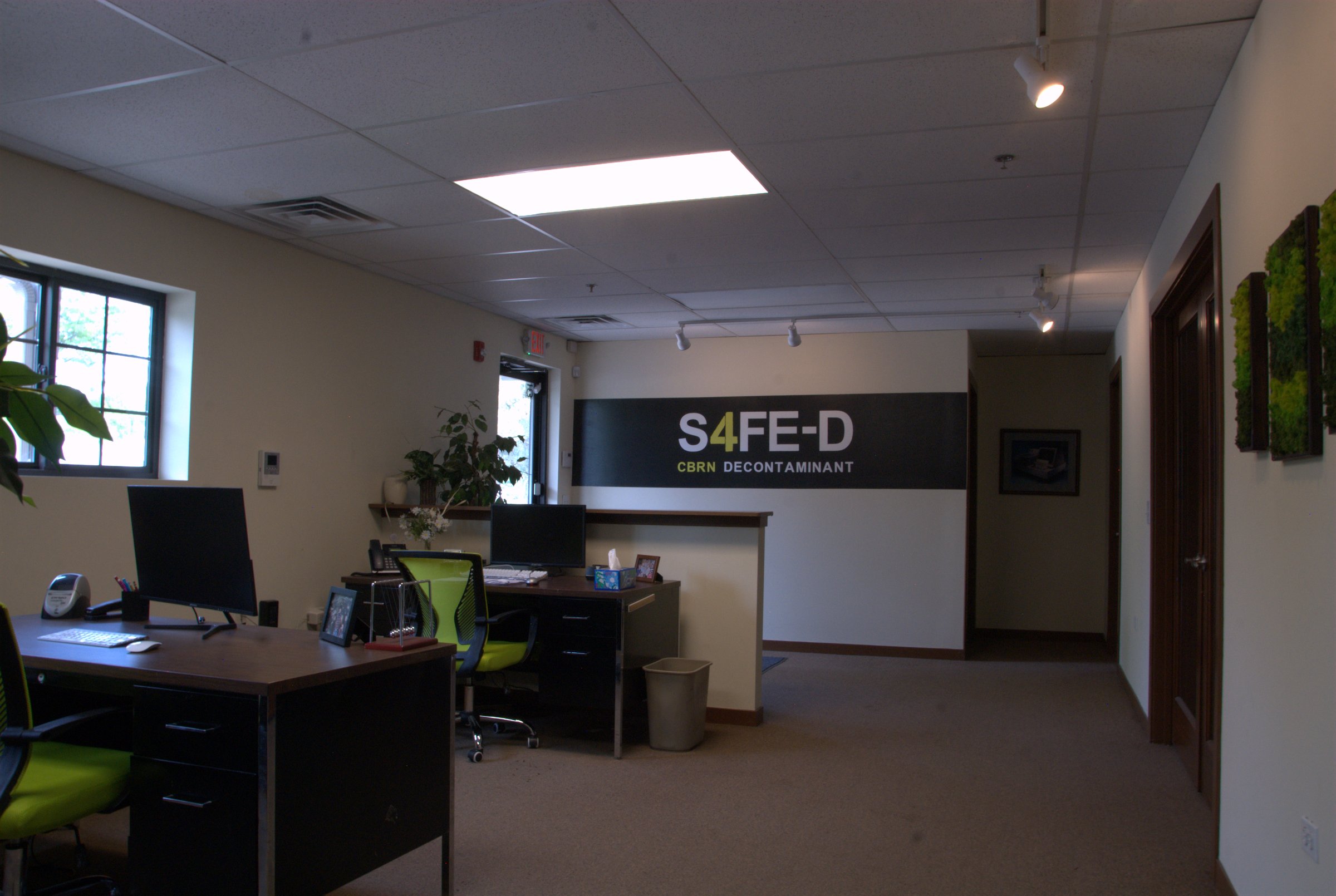 The Laboratory Technologies office in Elburn, Illinois — a desk with monitor and keyboard in the foreground, the S4FE-D&reg; CBRN Decontaminant mural on the back wall