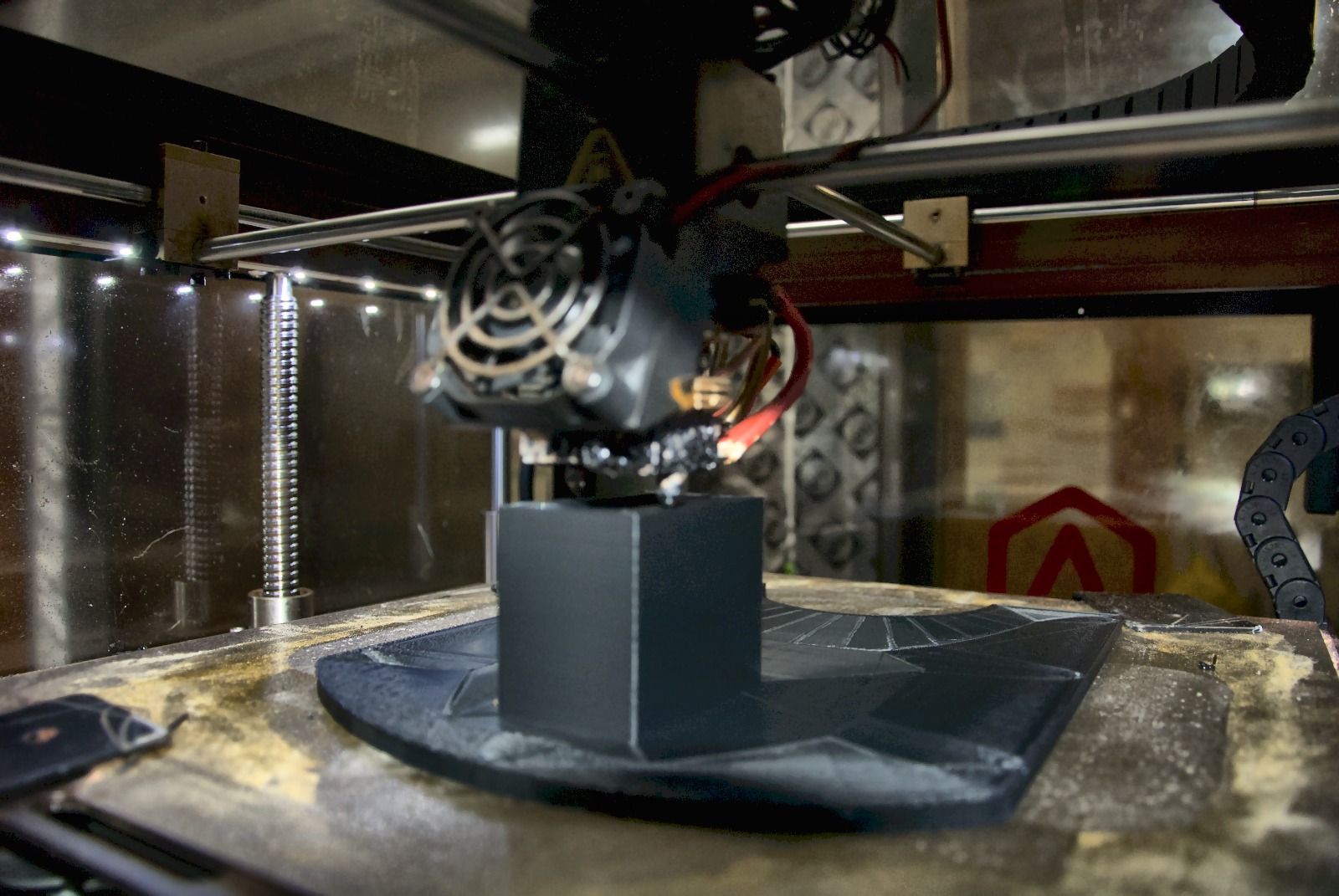 Wider view of the Raise3D Pro 2 build chamber during a Wiper Gold housing print, with the build plate, heated bed, and red filament feed visible in the LTI shop