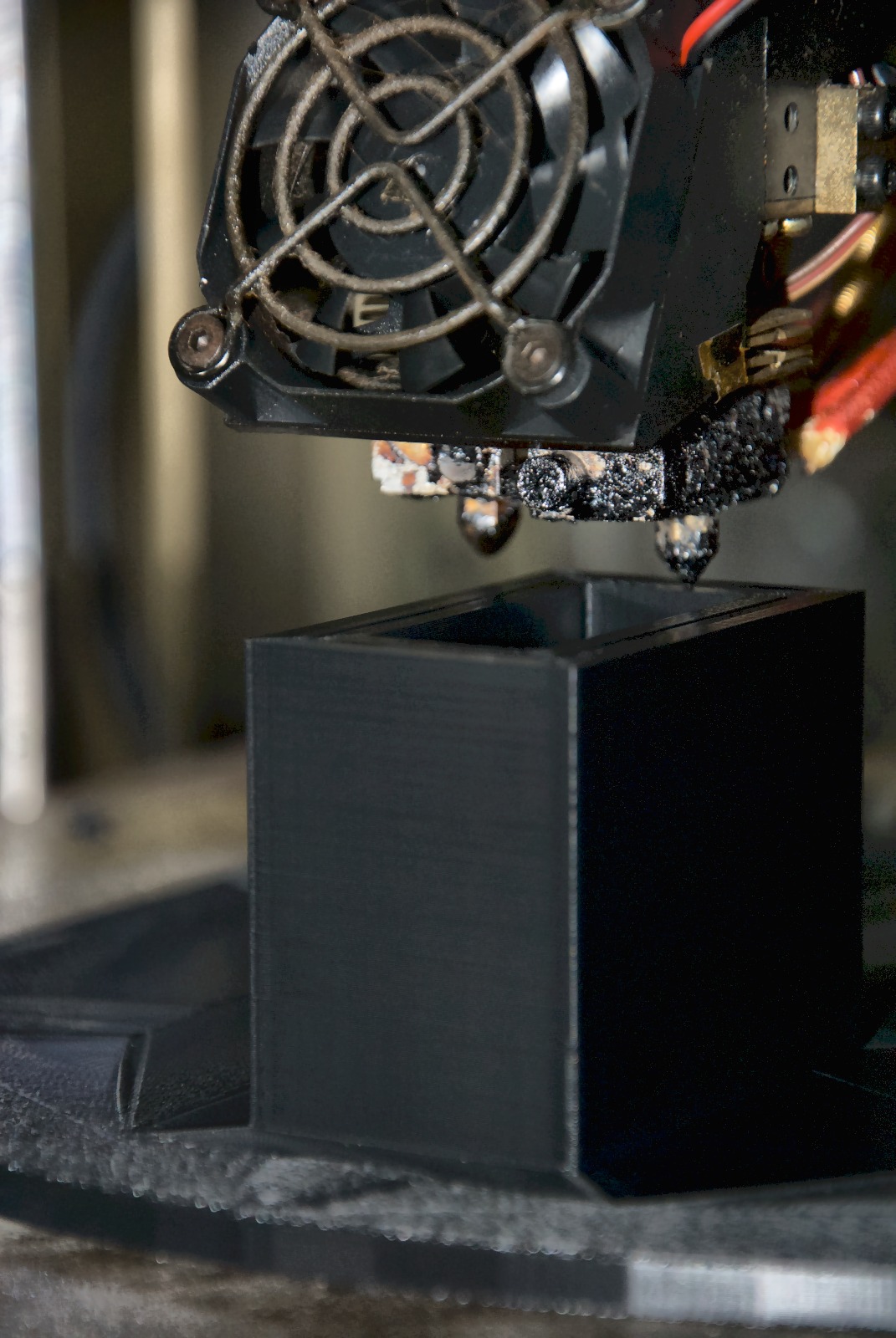 Close-up of the Raise3D Pro 2 print head, mid-print, building a black thermoplastic detector housing in the LTI shop in Elburn, Illinois