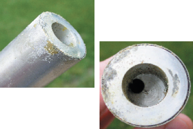 Two views of a destroyed LTI detector well — left: side view of an aluminum well housing showing exterior corrosion and crystallized residue; right: top-down view into the well showing a hole eaten through the floor of the well with hardened crystallized residue around the perimeter, caused by a competitor's commercially-sold radioactive decontamination product