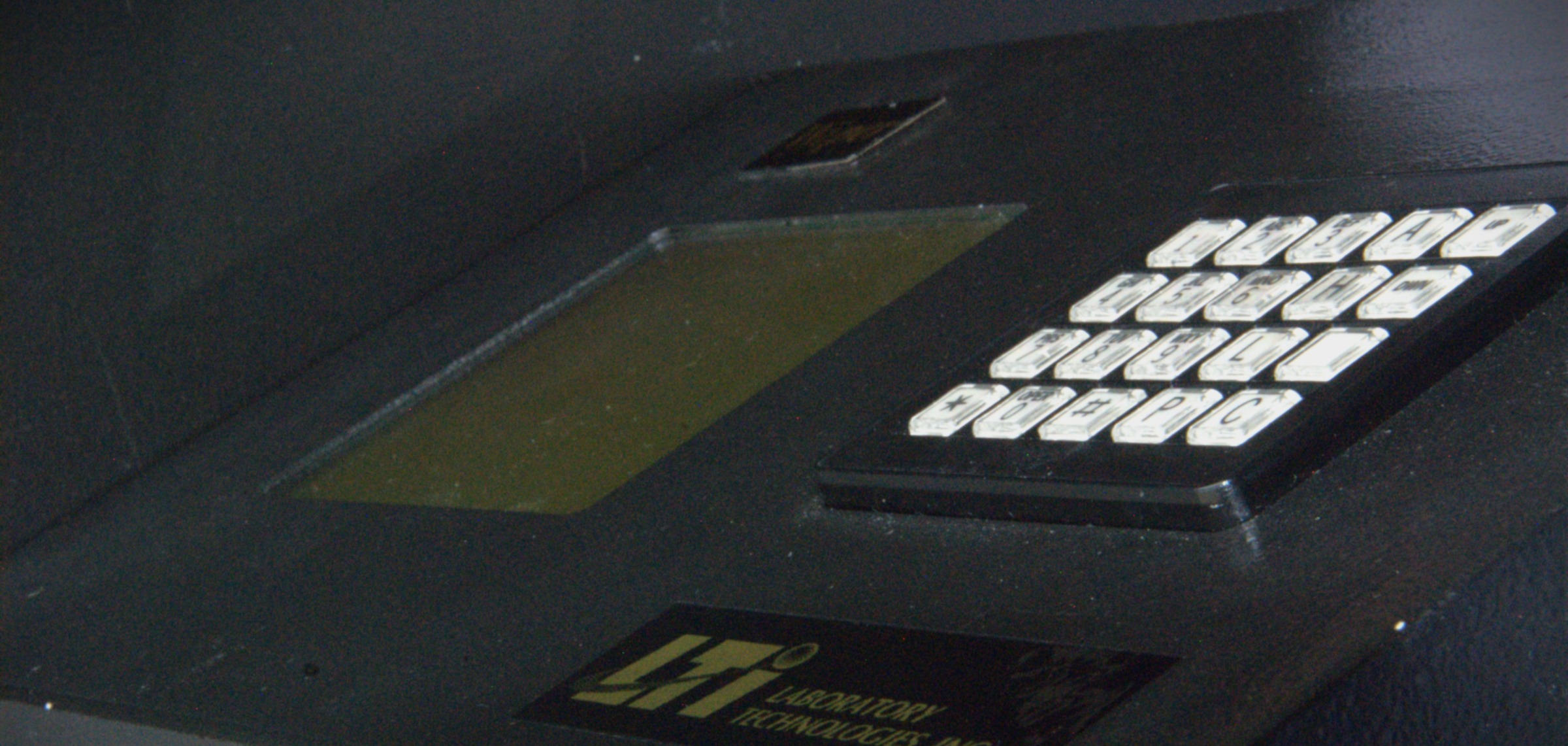 Detail of the Multi-Wiper control panel — backlit LCD with green phosphor, metallic keypad, gold LTI Laboratory Technologies, Inc. nameplate, all under low-key lighting